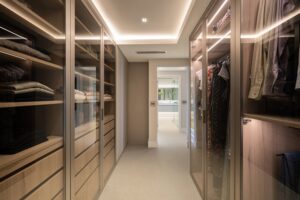 Modern walk-in closet with glass doors and warm lighting.