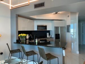 Modern kitchen with black countertops, stainless appliances, and bar stools.